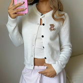 Person wearing a white cardigan with a teddy bear patch, holding a pink phone.